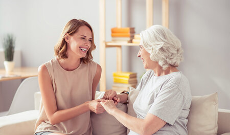 Pflegerin und Seniorin lächeln sich zu Hause an