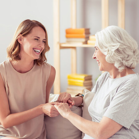 Pflegerin und Seniorin lächeln sich zu Hause an